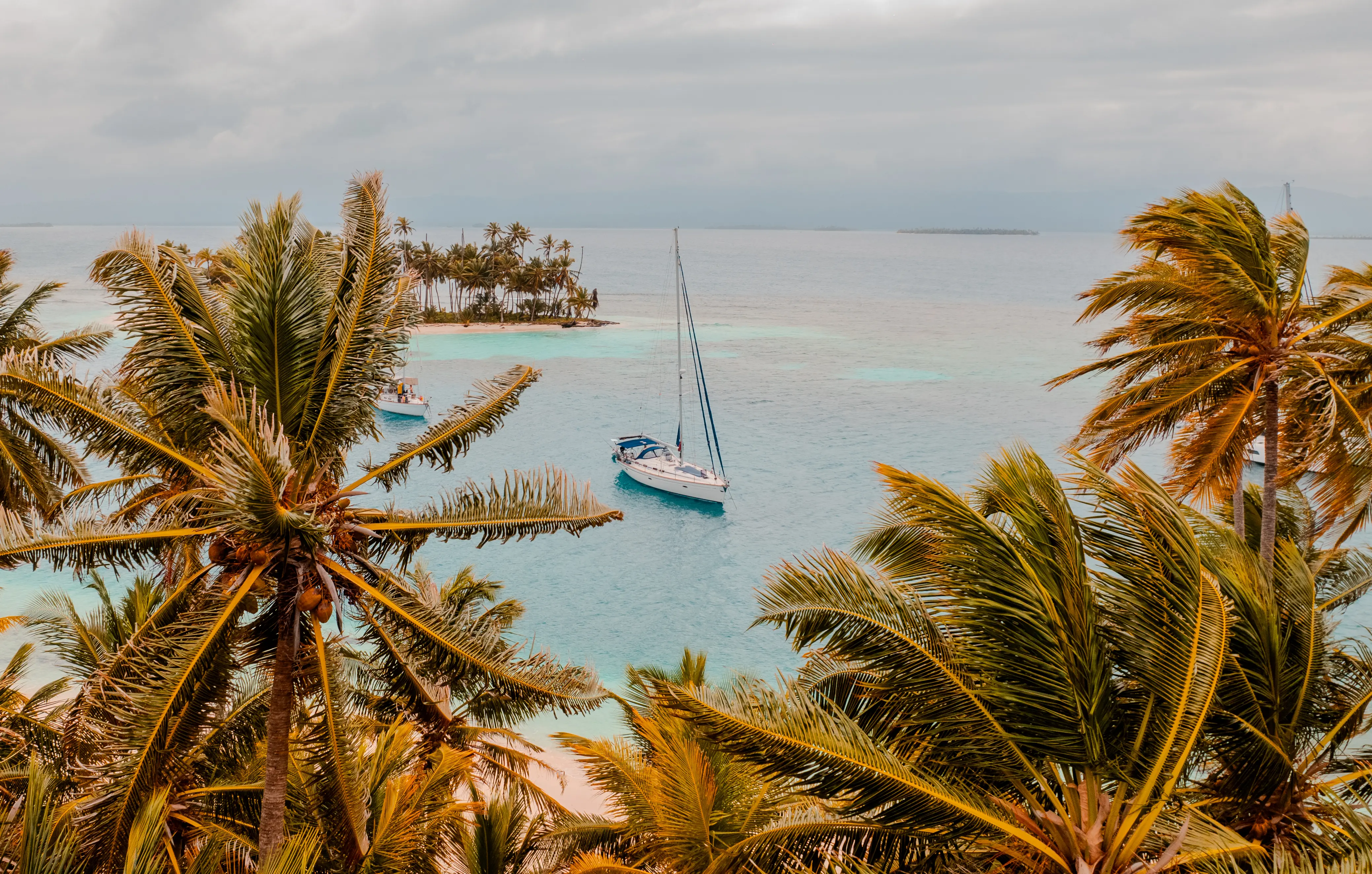 Veleros fondeados entre palmeras y pequeñas islas en aguas turquesas.