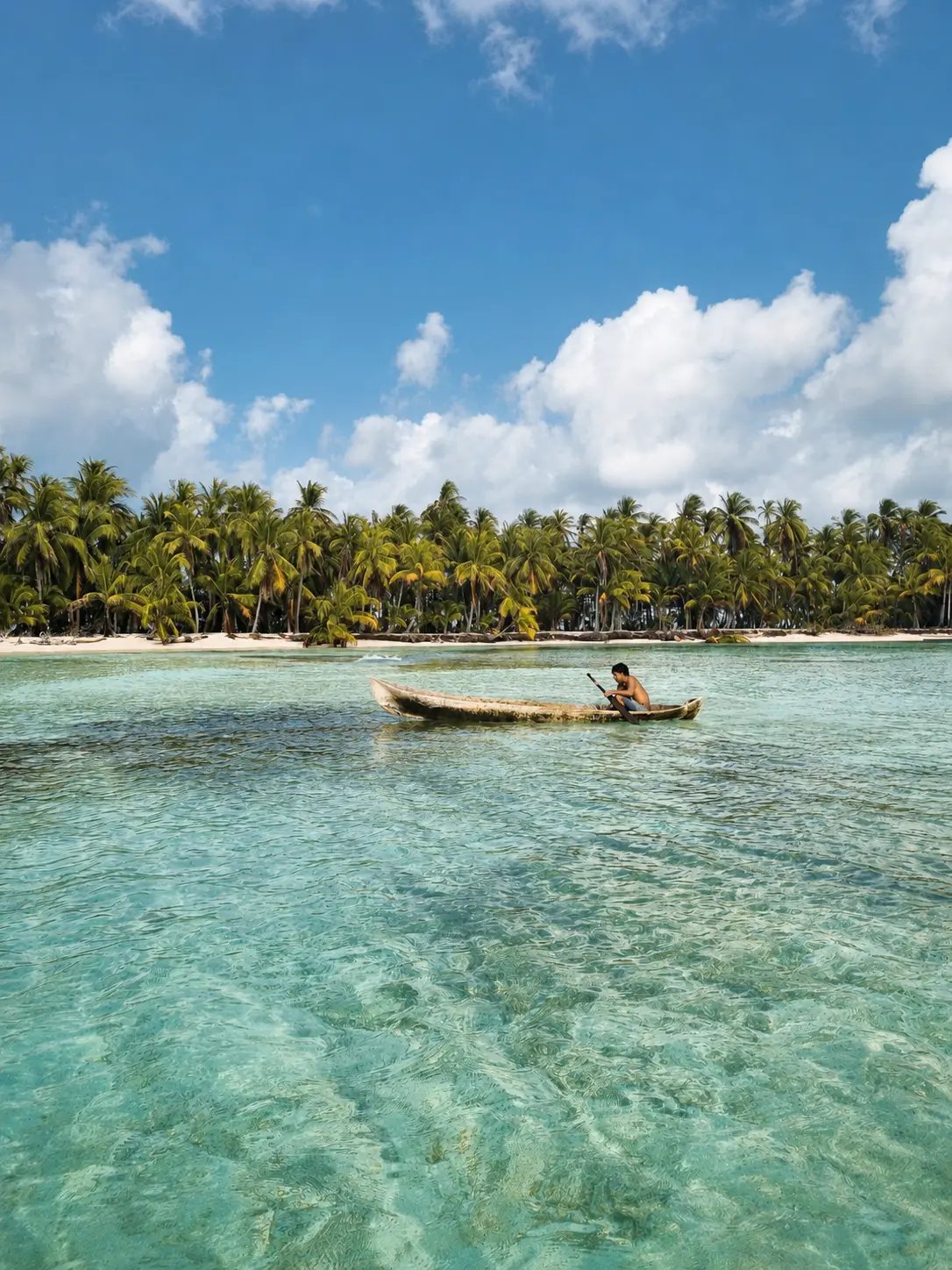 Persona remando una canoa tradicional frente a una isla de palmeras.